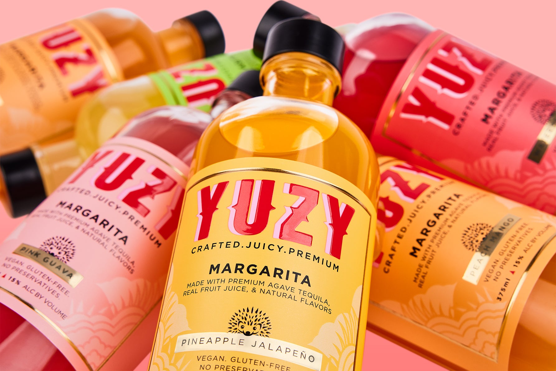 Bottles of YUZY Margaritas with colorful labels on a pink background.