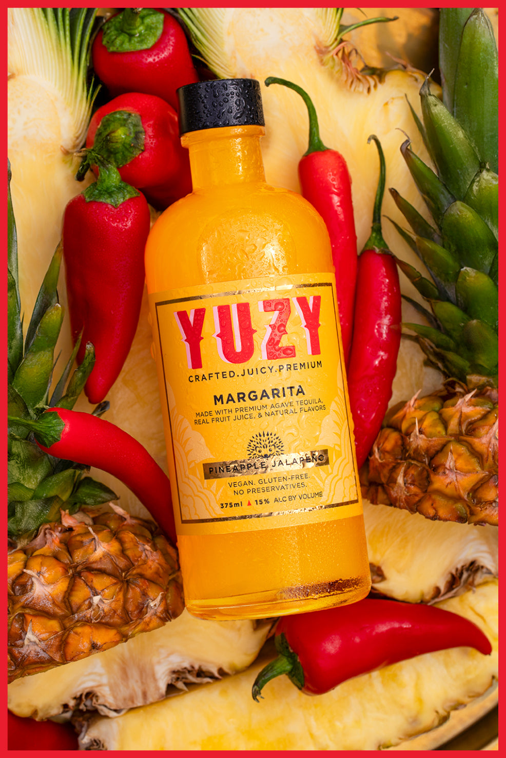 Bottle of YUZY "Pineapple Jalapeno" Margarita surrounded by red peppers and pineapples with a red border